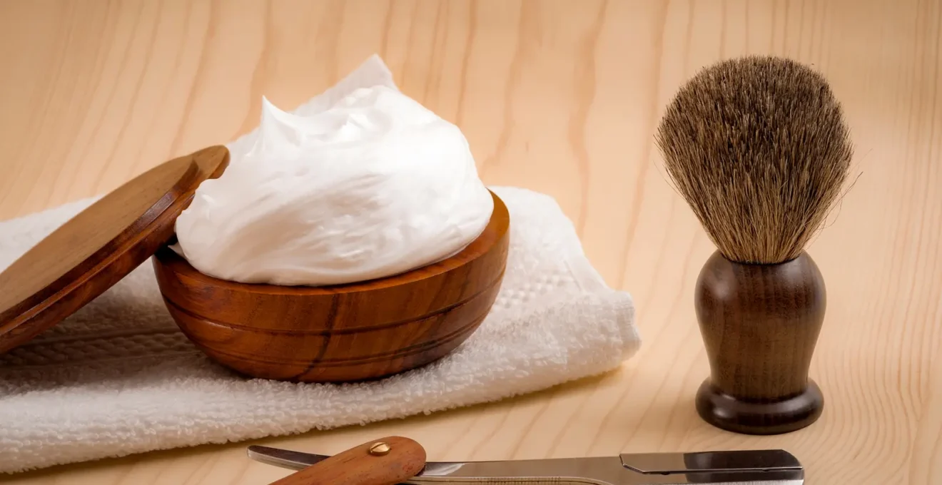 Flacon de soin après-rasage ambré, serviette blanche et rasoir coupe-choux entretenu disposés sur une surface en bois foncé